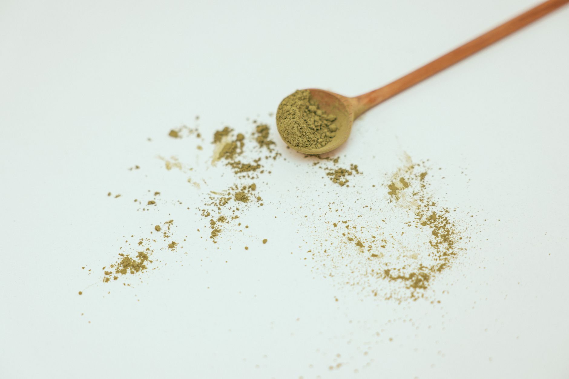 Flat lay image of organic matcha powder with wooden spoon on a clean white background.